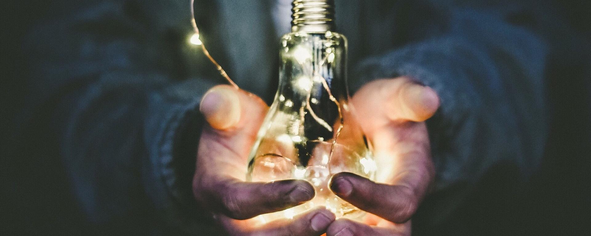 A pair of hands holds a glowing lightbulb