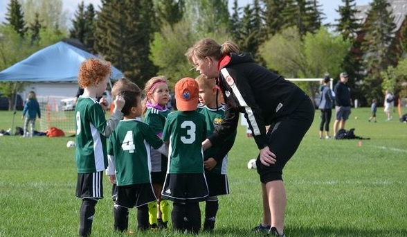 Kids in green jerseys on a soccer field, coached by Sue Miller