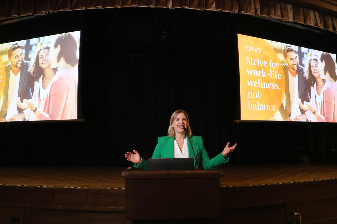 Laura Hambley stands in front of screens and behind a lecturn