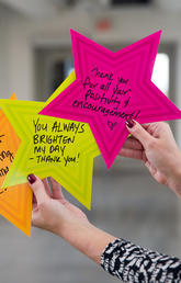 Woman's hands hold up three brightly coloured Givin' Thanks stars with positive messages written on them. 