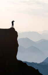 Person standing on edge of a cliff looking at mountains