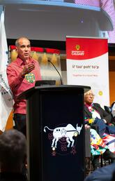A man stands behind a podium and gives a speech with two Indigenous elders sitting next to him