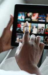 A hand scrolls through Netflix on a tablet
