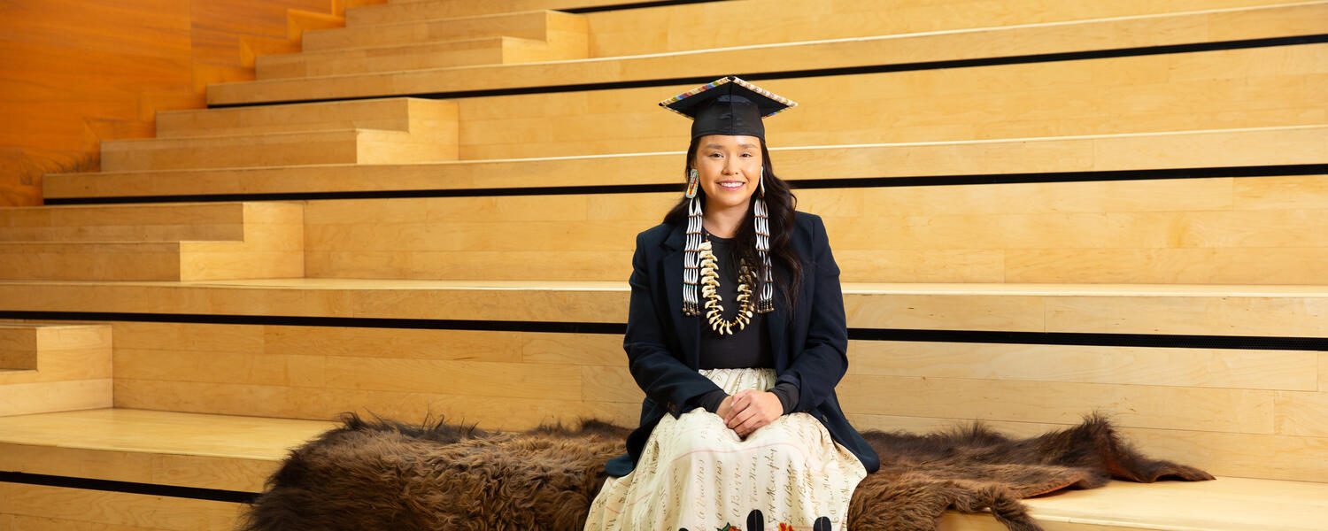 Indigenous student sitting on stairs with cap and gown