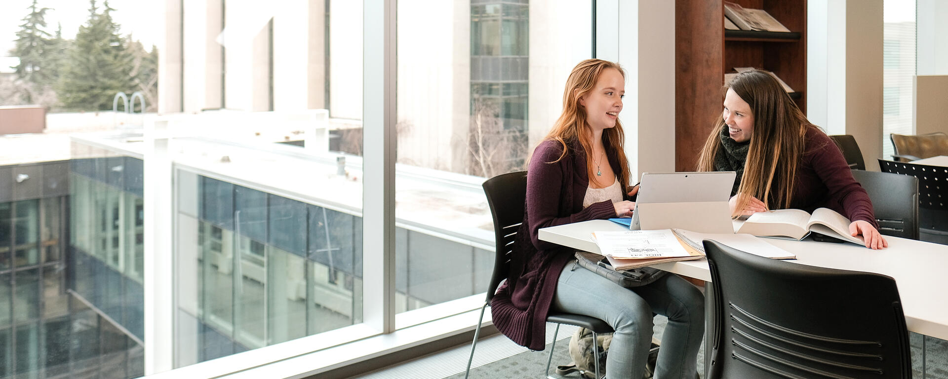 students sitting at table working with laptops and books