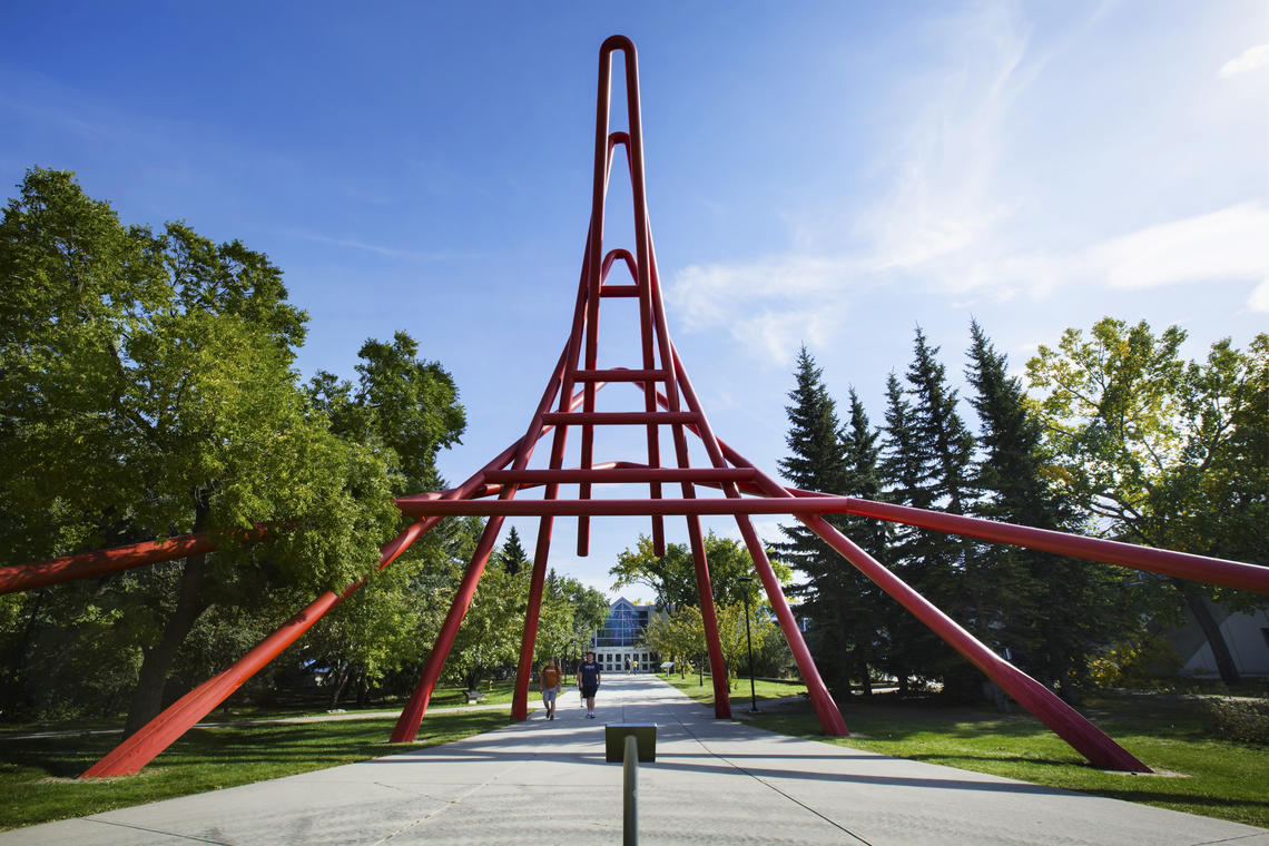 Picture of a sidewalk crossing underneath a large red sculpture