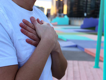Image of man's chest in white t-shirt, with hands crossed and pressed flat against chest