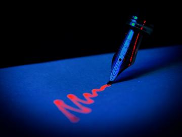 Image of pen drawing squiggly line in glowing red ink on a blue surface