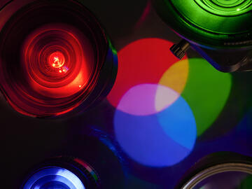 A photo featuring camera lenses illuminated in red, green, and blue light, with colorful reflections blending into overlapping patterns.