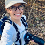 Amanda Melin in field gear in Costa Rica holding a DSLR camera with a zoom lens