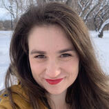 Headshot of a woman with long brown hair and brown eyes in a yellow parka against a snowy backdrop.
