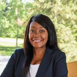 A headshot of a Black women smiling and standing behind a scenic background