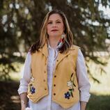 Dr. Melanie Griffith Brice is wearing a beaded Métis vest. She is standing in front of trees. 