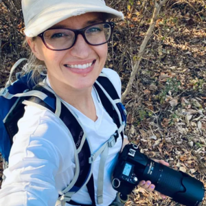 Amanda Melin in field gear in Costa Rica holding a DSLR camera with a zoom lens