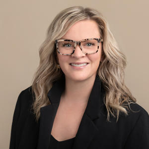 Headshot of Dr. MacEachern, who has pale skin, blonde hair, and is wearing glasses and a black suit jacket