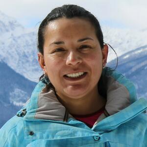 Headshot of a smiley woman with a blue jacket and mountains on the background